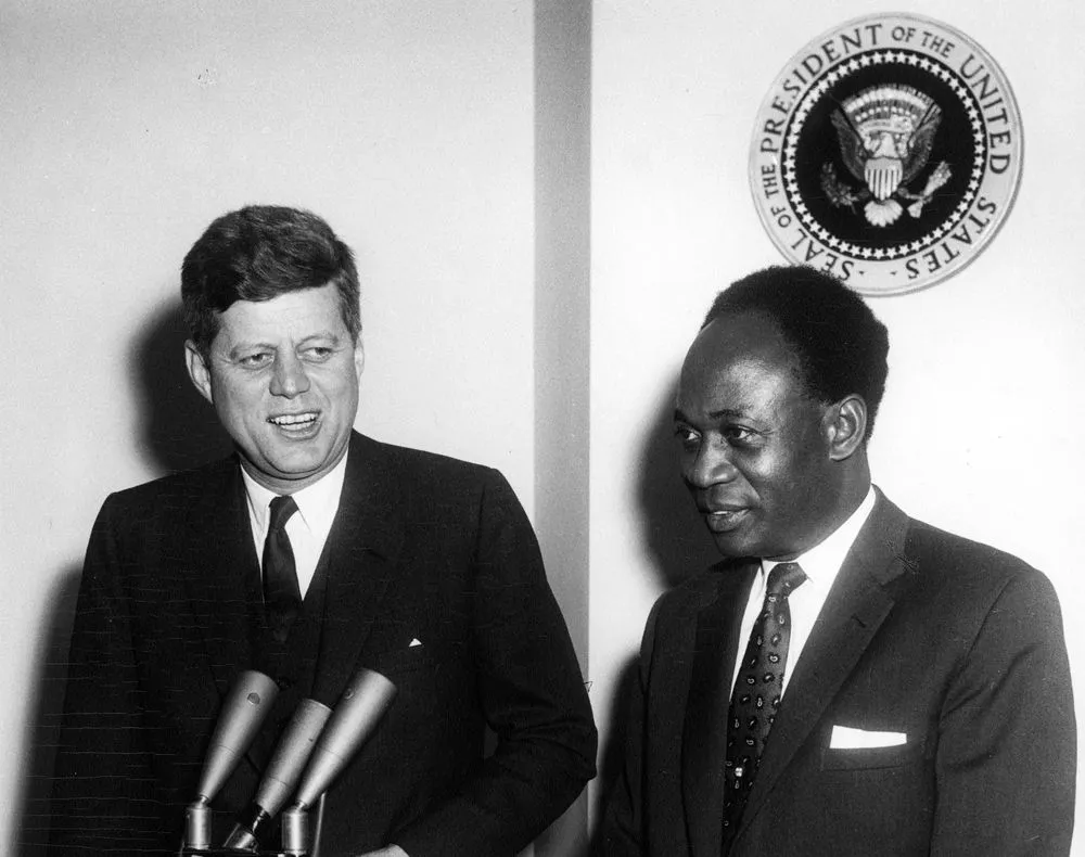 Kwame Nkrumah and President John F. Kennedy standing beside microphones, with the seal of the President of the United States on the wall behind them.